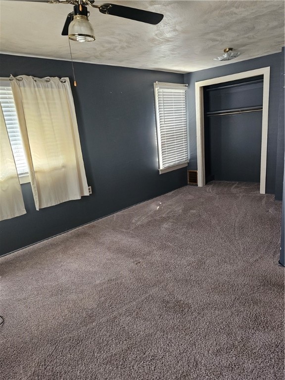 unfurnished bedroom with a textured ceiling, carpet, a closet, and multiple windows