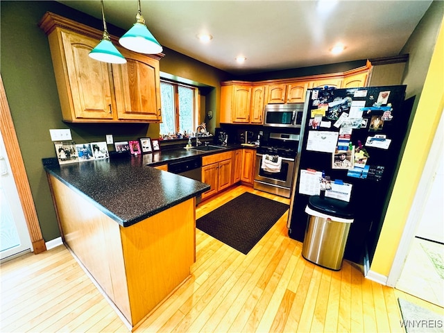 kitchen featuring hanging light fixtures, kitchen peninsula, sink, stainless steel appliances, and light wood-type flooring