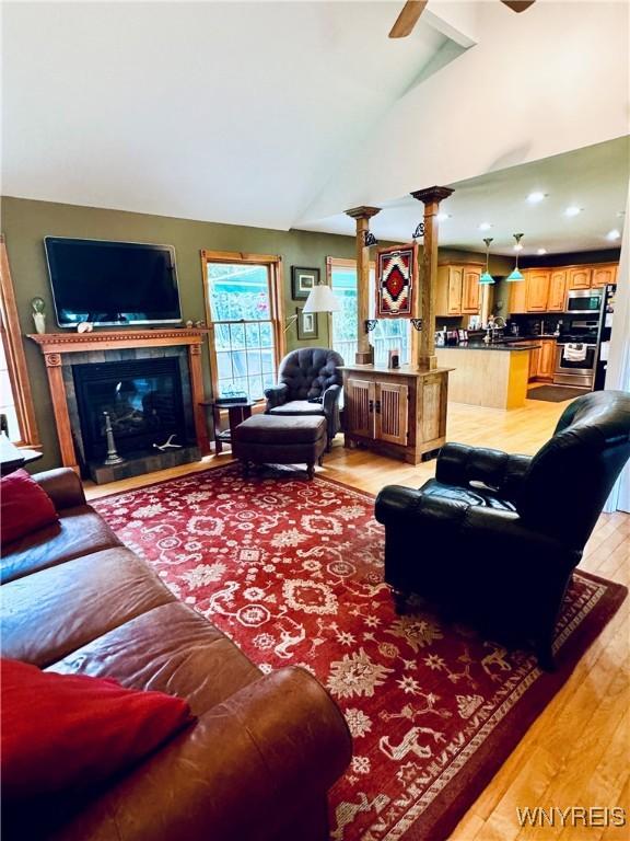 living room with ceiling fan, light wood-type flooring, ornate columns, and lofted ceiling