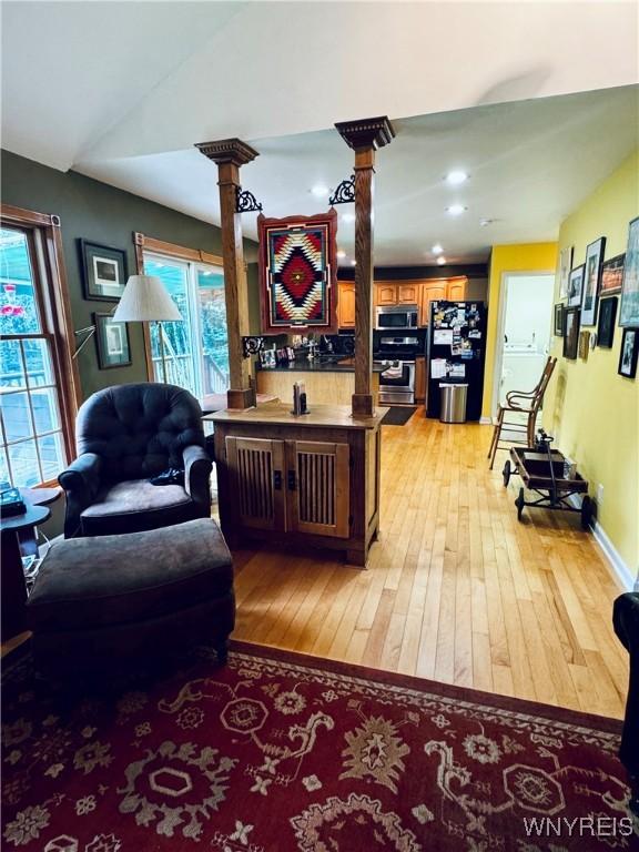 living room with light hardwood / wood-style floors, vaulted ceiling, and ornate columns