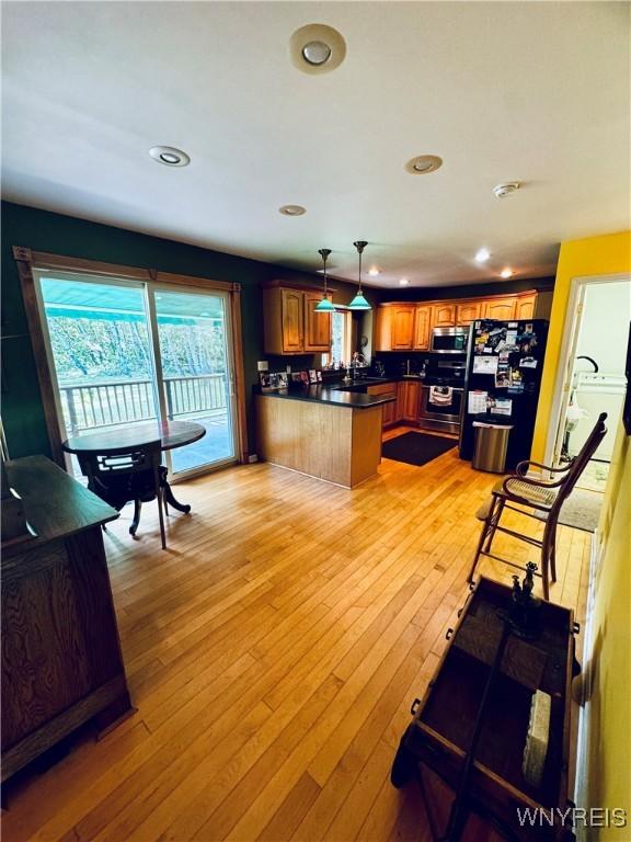 kitchen featuring kitchen peninsula, decorative light fixtures, light hardwood / wood-style flooring, appliances with stainless steel finishes, and a kitchen breakfast bar