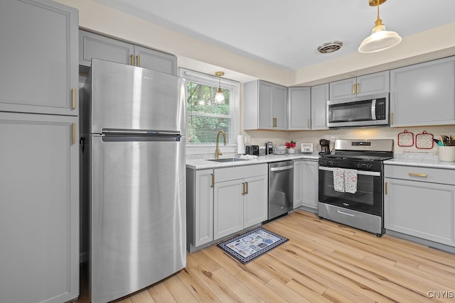 kitchen with gray cabinetry, decorative light fixtures, light hardwood / wood-style flooring, stainless steel appliances, and sink