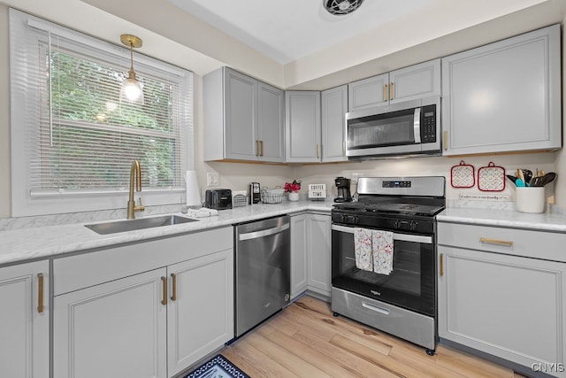 kitchen with light wood-type flooring, sink, decorative light fixtures, and appliances with stainless steel finishes