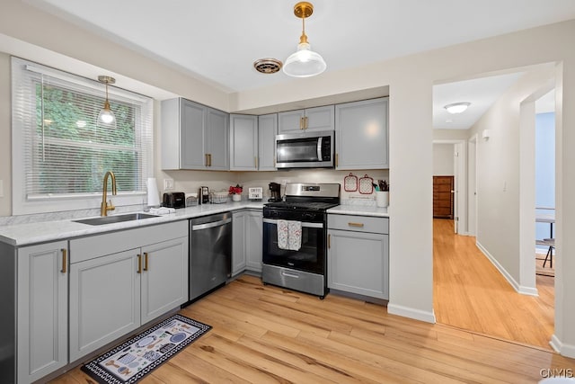 kitchen with gray cabinetry, stainless steel appliances, sink, and light wood-type flooring