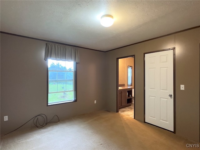 unfurnished bedroom featuring a textured ceiling, crown molding, ensuite bath, and light carpet