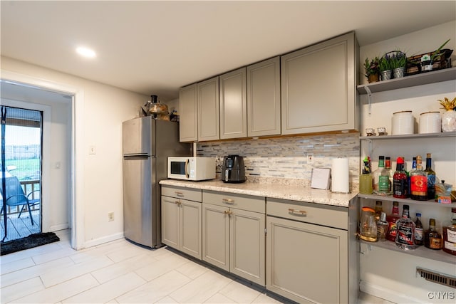 kitchen featuring stainless steel fridge, light stone countertops, gray cabinets, and tasteful backsplash