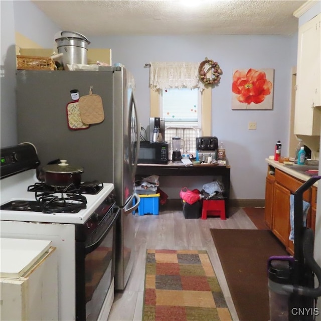 kitchen featuring white range with gas cooktop, a textured ceiling, white cabinets, and light hardwood / wood-style floors