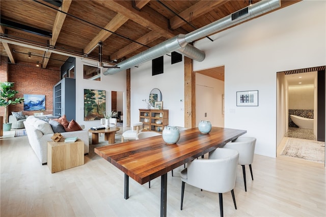 dining space featuring light wood-type flooring, wood ceiling, beam ceiling, and a high ceiling