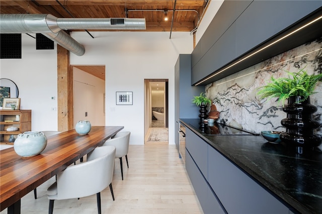 kitchen featuring dark stone countertops, black electric stovetop, a high ceiling, wooden ceiling, and light hardwood / wood-style floors