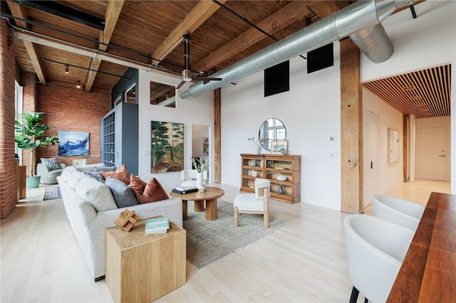 living room with brick wall, light hardwood / wood-style floors, wood ceiling, ceiling fan, and a towering ceiling