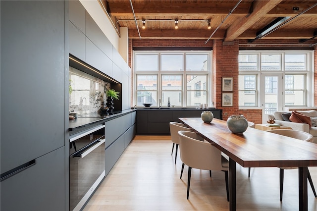 dining space with wood ceiling, brick wall, light wood-type flooring, and beam ceiling