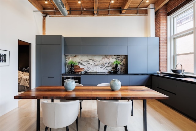 dining space with light wood-type flooring, sink, a towering ceiling, wood ceiling, and brick wall