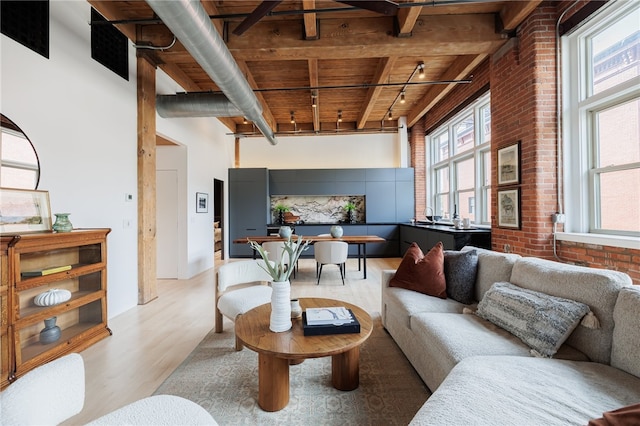 living room featuring brick wall, beamed ceiling, wooden ceiling, wood-type flooring, and a high ceiling