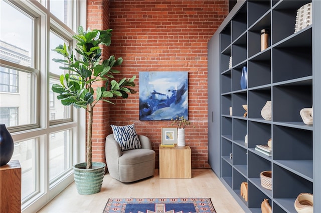 sitting room with brick wall, a healthy amount of sunlight, and light hardwood / wood-style flooring