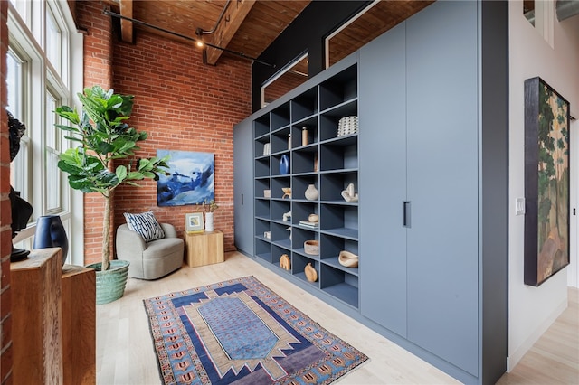 living area with beamed ceiling, a towering ceiling, wood ceiling, brick wall, and light hardwood / wood-style floors