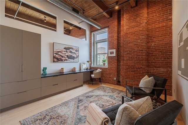 living area with brick wall, wooden ceiling, beam ceiling, a high ceiling, and light wood-type flooring