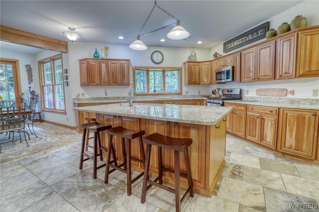 kitchen featuring light stone countertops, decorative light fixtures, a kitchen island with sink, a breakfast bar, and appliances with stainless steel finishes