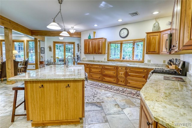 kitchen featuring a center island with sink, sink, decorative light fixtures, light stone counters, and range