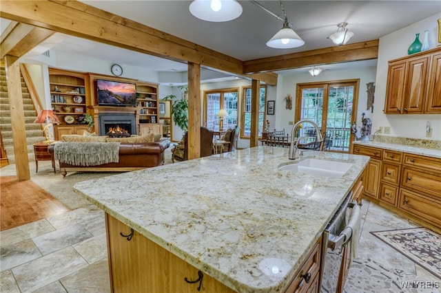 kitchen with a kitchen island with sink, sink, hanging light fixtures, light stone countertops, and beamed ceiling