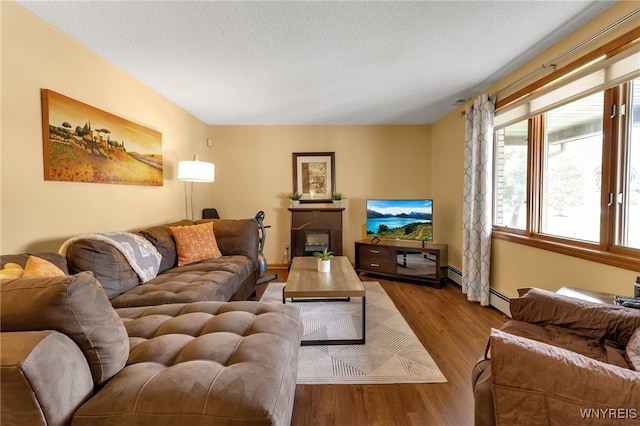 living room with a baseboard heating unit, light hardwood / wood-style flooring, and a textured ceiling