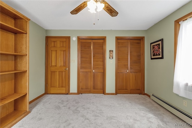 unfurnished bedroom with a baseboard heating unit, ceiling fan, light colored carpet, and multiple closets