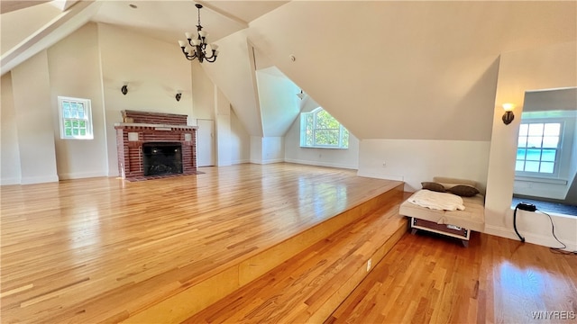 unfurnished living room with a chandelier, lofted ceiling, a fireplace, and light hardwood / wood-style flooring