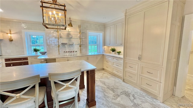 kitchen with pendant lighting, decorative backsplash, crown molding, and cream cabinetry