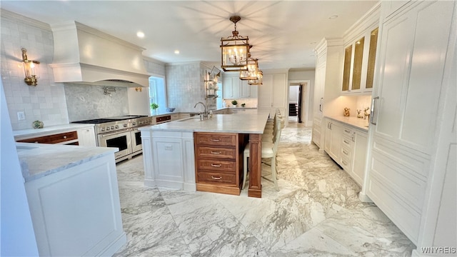 kitchen featuring tasteful backsplash, premium range hood, decorative light fixtures, double oven range, and white cabinetry