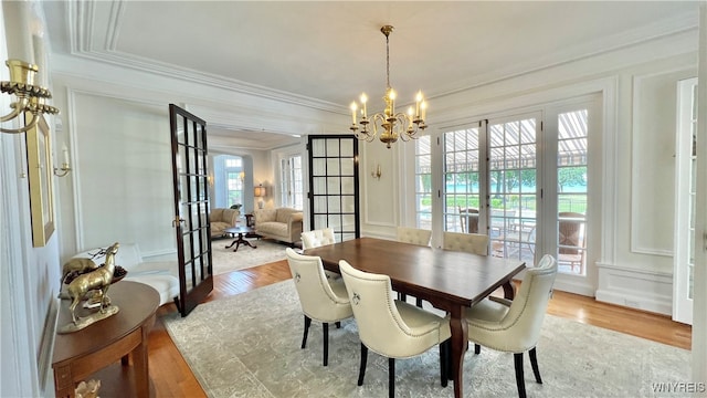 dining area featuring light hardwood / wood-style floors, an inviting chandelier, ornamental molding, and french doors