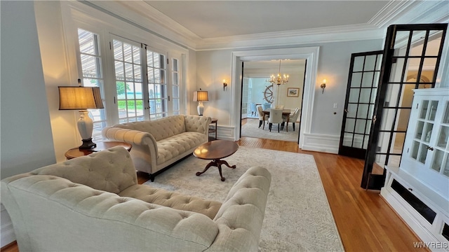 living room featuring french doors, light hardwood / wood-style floors, an inviting chandelier, and crown molding