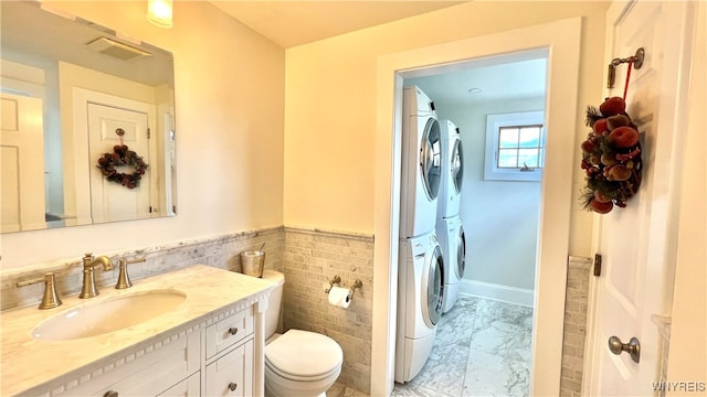 bathroom with vanity, toilet, tile walls, and stacked washer and clothes dryer