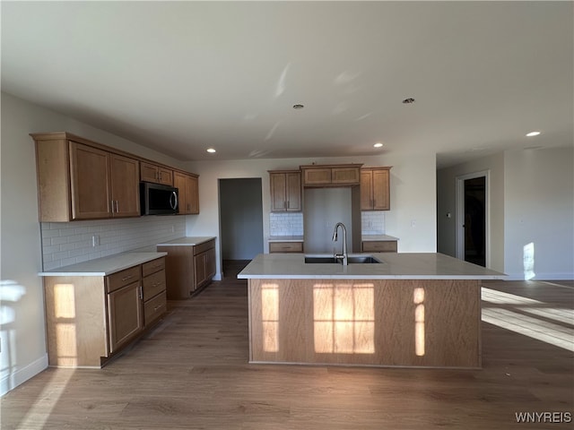 kitchen featuring sink, backsplash, hardwood / wood-style flooring, and a kitchen island with sink