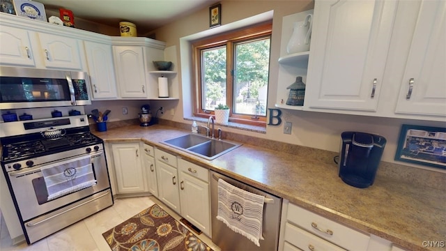 kitchen with appliances with stainless steel finishes, sink, light tile patterned floors, and white cabinets