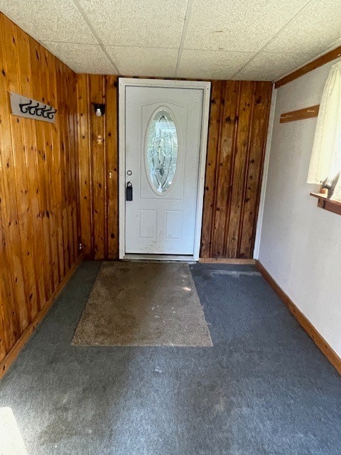 foyer with a drop ceiling, wooden walls, and carpet floors