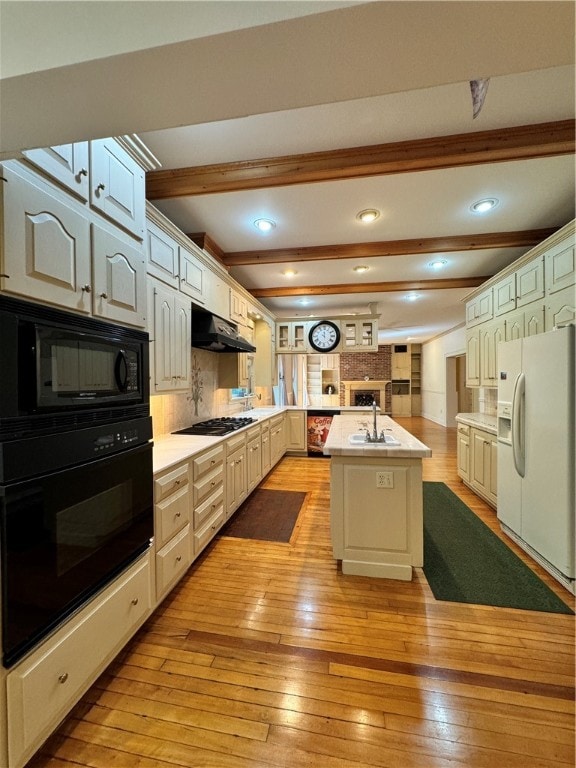 kitchen featuring black appliances, light hardwood / wood-style flooring, an island with sink, tasteful backsplash, and beamed ceiling