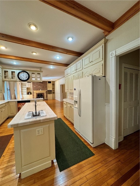 kitchen with tile countertops, light hardwood / wood-style floors, white refrigerator with ice dispenser, and sink