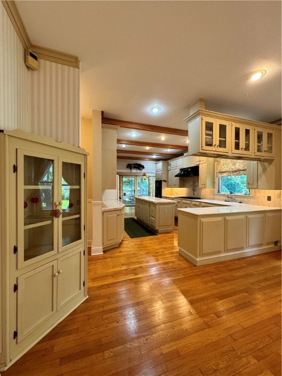 kitchen with kitchen peninsula, light wood-type flooring, tasteful backsplash, white gas stovetop, and cream cabinets