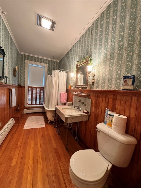 bathroom featuring a baseboard heating unit, crown molding, hardwood / wood-style floors, wood walls, and toilet