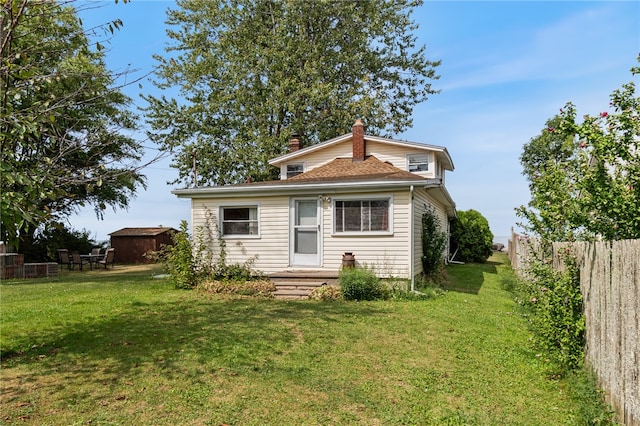 rear view of property featuring a lawn and a storage unit