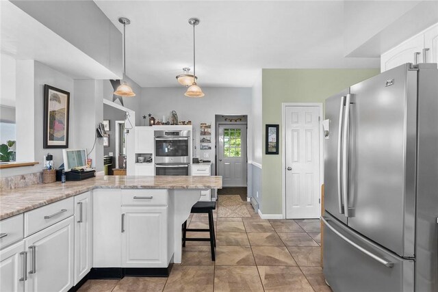 kitchen with appliances with stainless steel finishes, decorative light fixtures, kitchen peninsula, and white cabinets