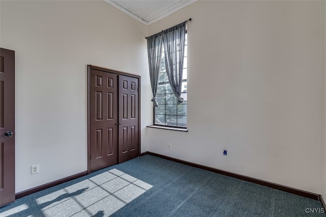 empty room featuring ornamental molding, a wealth of natural light, and dark colored carpet