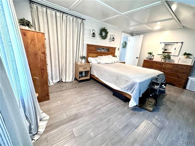 bedroom with coffered ceiling, light wood-type flooring, and wooden walls