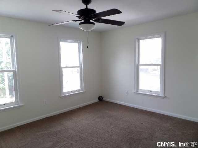 unfurnished room featuring baseboards, dark carpet, and a ceiling fan