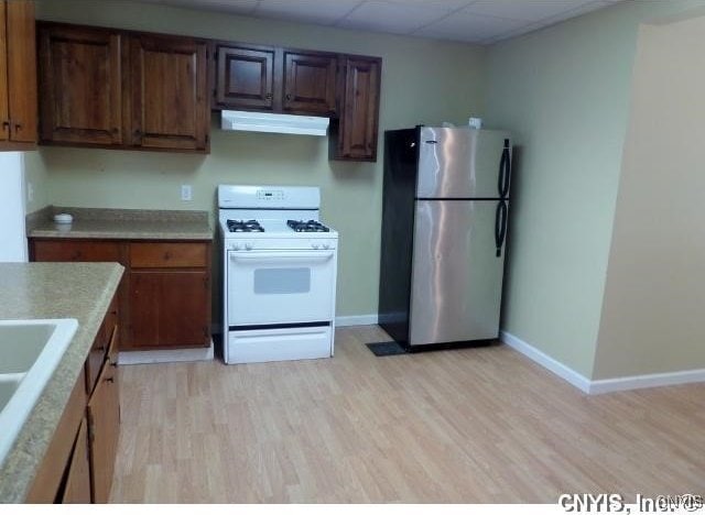 kitchen with white gas stove, light countertops, light wood-style floors, freestanding refrigerator, and under cabinet range hood