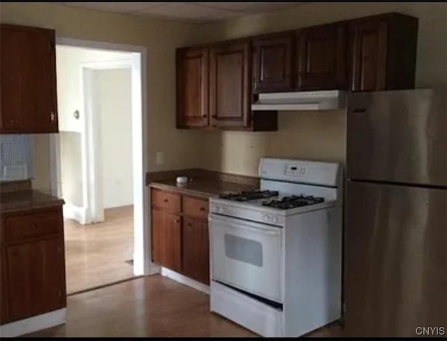 kitchen featuring under cabinet range hood, light wood-type flooring, freestanding refrigerator, brown cabinets, and gas range gas stove