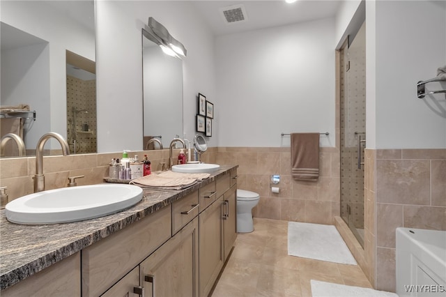 bathroom with toilet, tile patterned floors, a shower with door, vanity, and tile walls