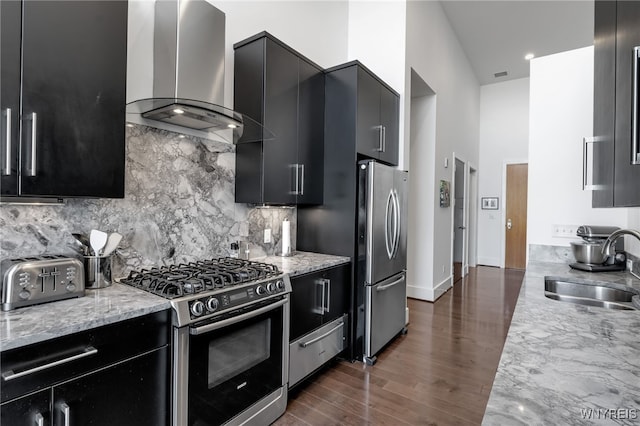 kitchen featuring appliances with stainless steel finishes, light stone counters, sink, wall chimney range hood, and dark wood-type flooring