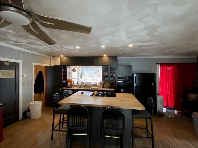 kitchen with a breakfast bar, black appliances, butcher block counters, and wood finished floors