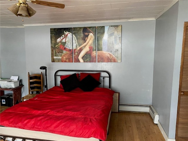 bedroom featuring crown molding, baseboards, wood finished floors, and a baseboard radiator