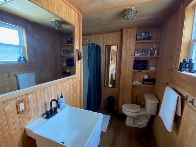 bathroom with wooden walls, a sink, toilet, a shower with shower curtain, and wood finished floors
